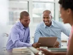 A group of men are sitting at a table looking at a laptop.
