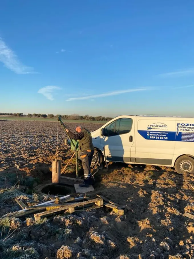Persona con camisa azul trabajando dentro de un pozo circular, posiblemente cavando. El pozo tiene paredes que parecen ladrillos.