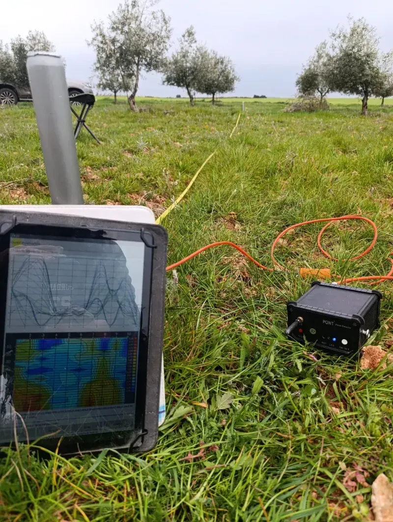 Un camión con grúa trabajando cerca de un pozo circular abierto en un campo de árboles bajo un cielo azul.