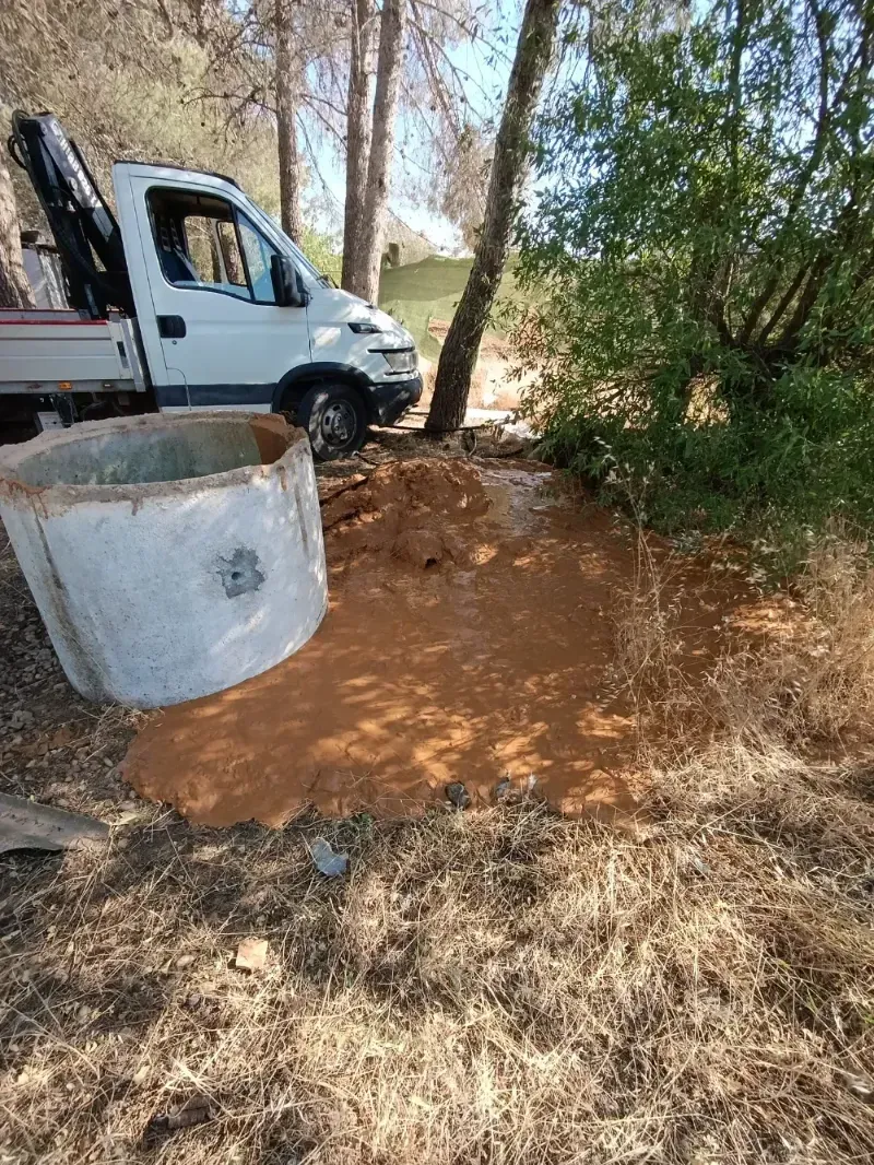 Un charco fangoso de líquido marrón estalla cerca de un camión blanco y un pozo de concreto en un área boscosa.