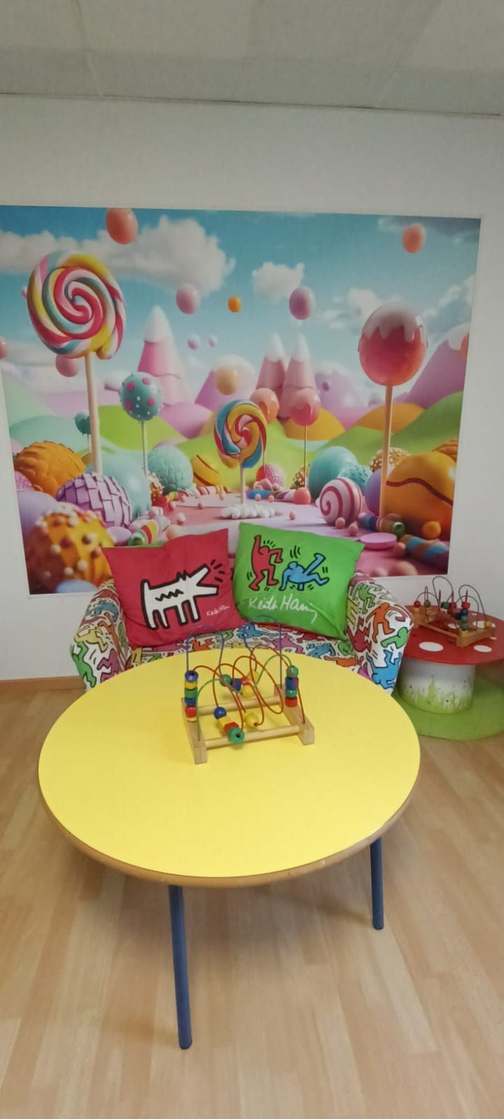 Una habitación con una mesa amarilla y una imagen de piruletas en la pared.