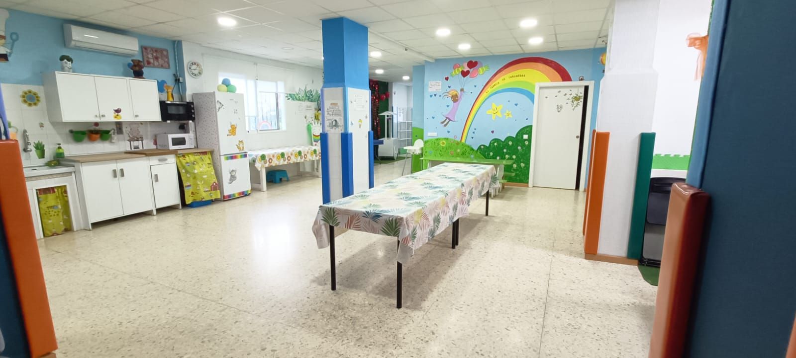 Una habitación grande con una mesa y un arco iris pintado en la pared.