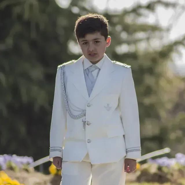 Un niño lleva un traje blanco y corbata.