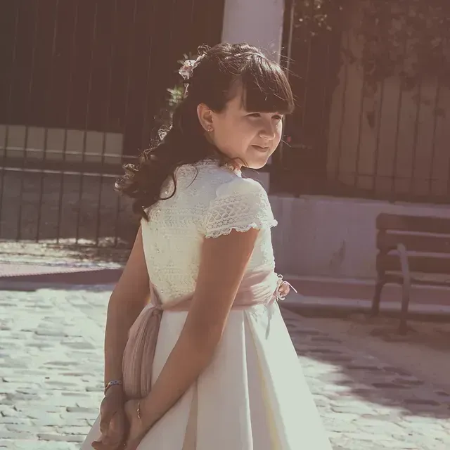 Una niña con un vestido blanco está parada en una calle adoquinada.