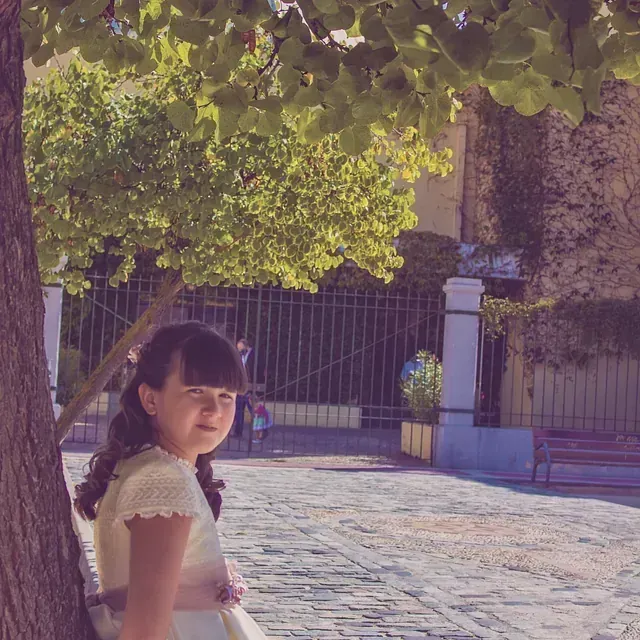 Una niña con un vestido blanco está apoyada contra un árbol.
