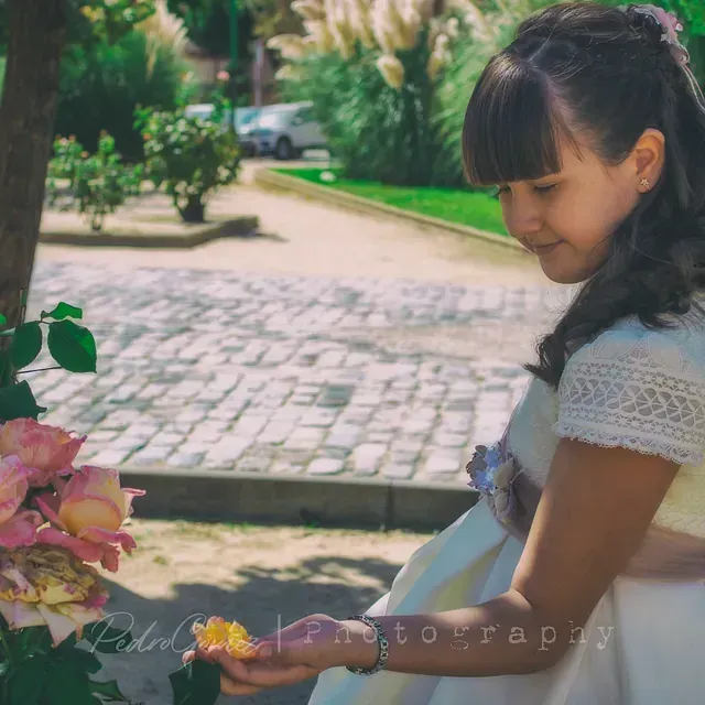 Una niña con un vestido blanco sostiene una flor en sus manos.