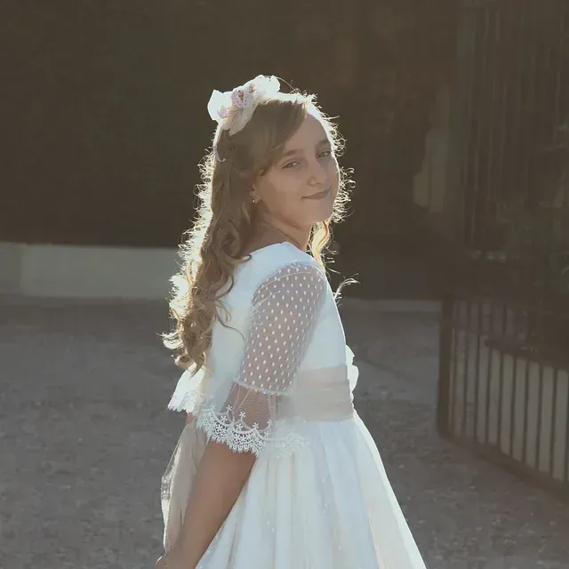 Una niña con un vestido blanco y una flor en el pelo.