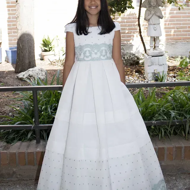 Una niña con un vestido blanco y una cinta azul alrededor de la cintura.