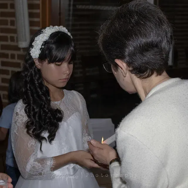Una mujer con un vestido blanco sostiene una vela.