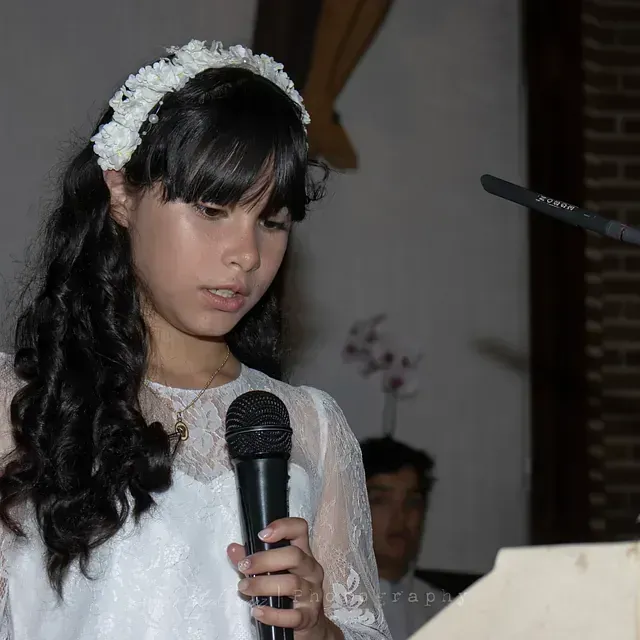 Una chica con un vestido blanco sostiene un micrófono.