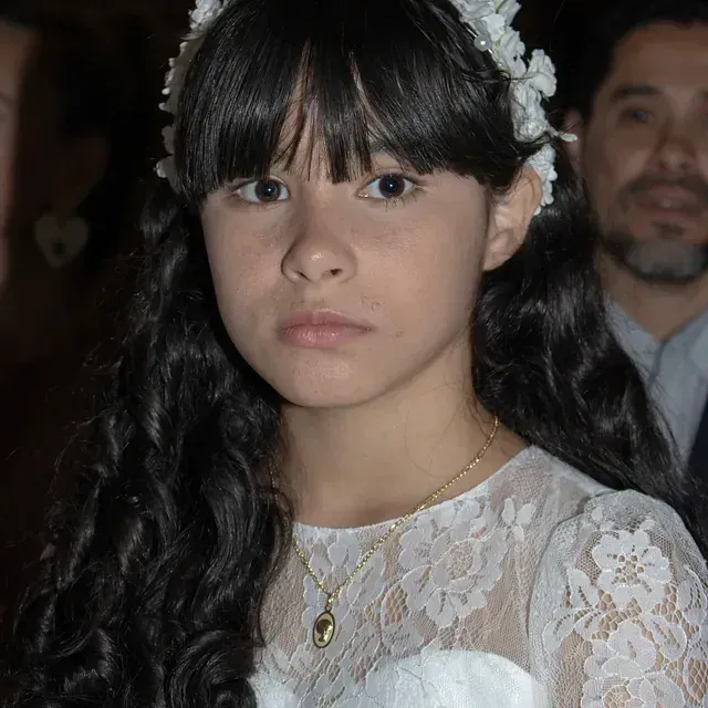 Una niña con un vestido blanco y una flor en el pelo.