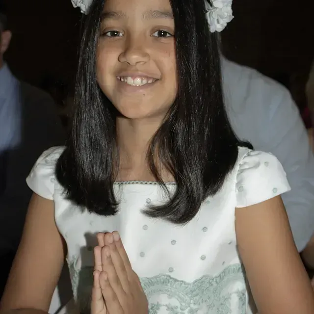 Una niña con un vestido blanco y una flor en el pelo.