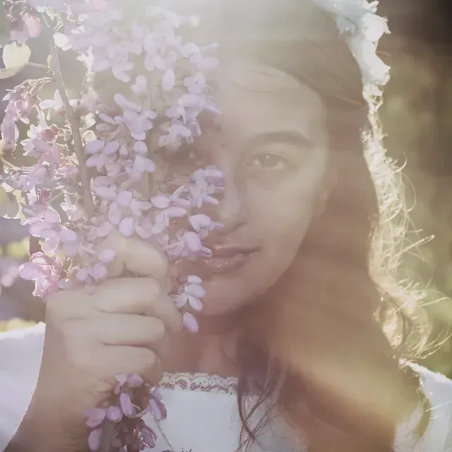 Una mujer sostiene flores moradas frente a su cara.
