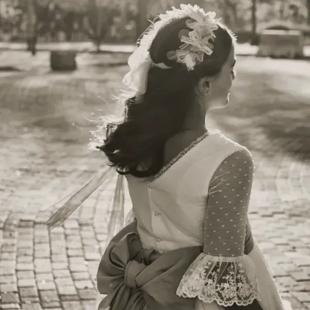 Una fotografía en blanco y negro de una niña con un vestido blanco y una flor en el pelo.