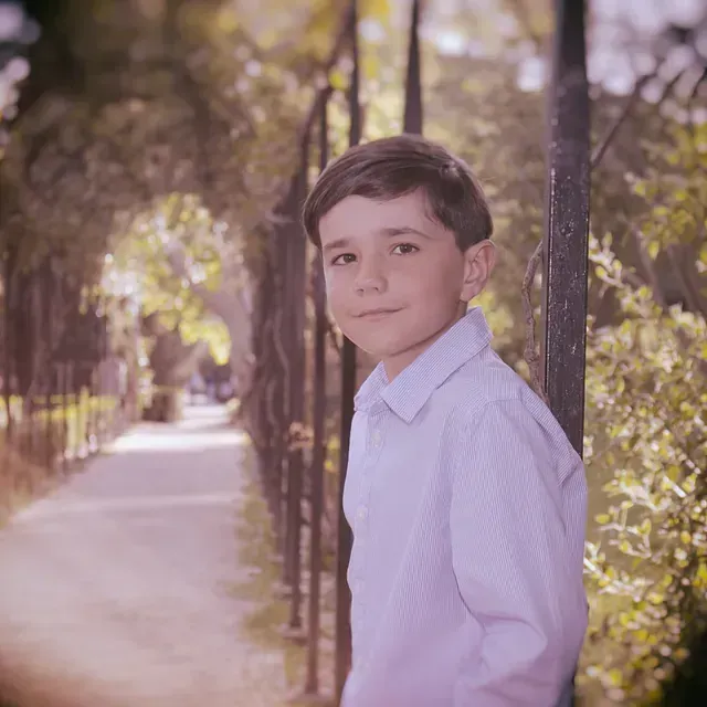 Un niño pequeño está apoyado contra un árbol en un parque.