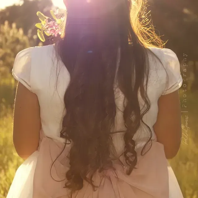 Una niña con un vestido blanco y un lazo rosa en la espalda.