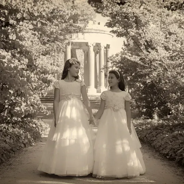Dos niñas con vestidos blancos caminan por un sendero tomadas de la mano.