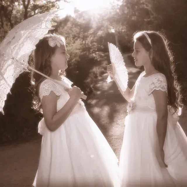 Dos niñas con vestidos blancos sosteniendo paraguas y abanicos