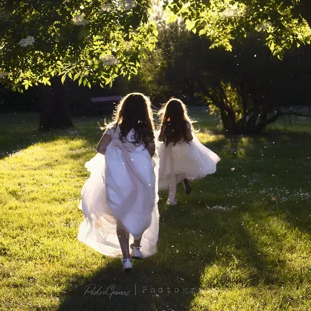 Dos niñas con vestidos blancos corren por la hierba.