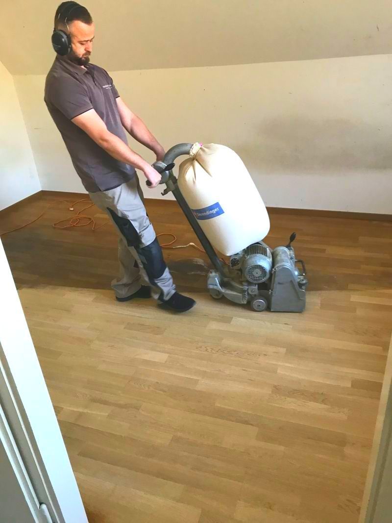 Ein Mann schleift mit einer Maschine einen Holzboden. Foto von der SAG GmbH