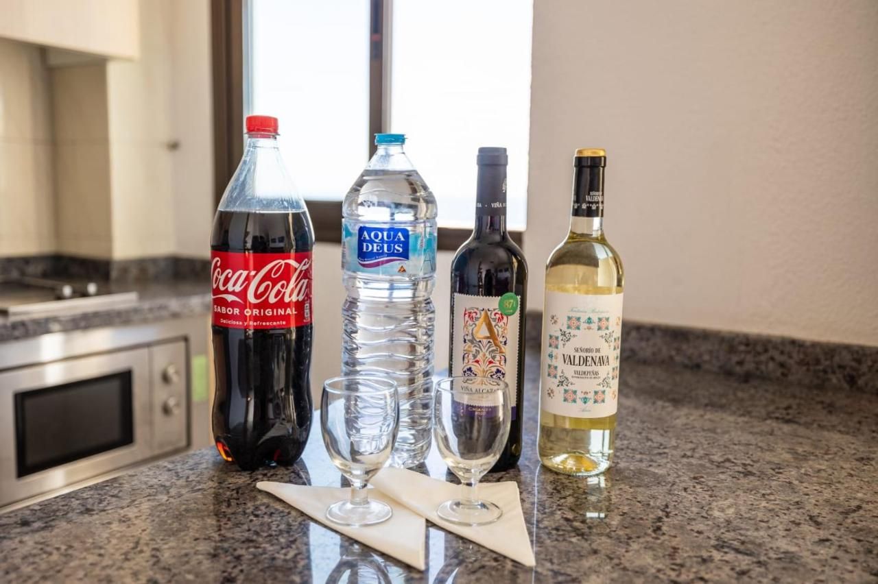 Una botella de Coca Cola, una botella de agua y dos copas de vino están en la encimera de la cocina.