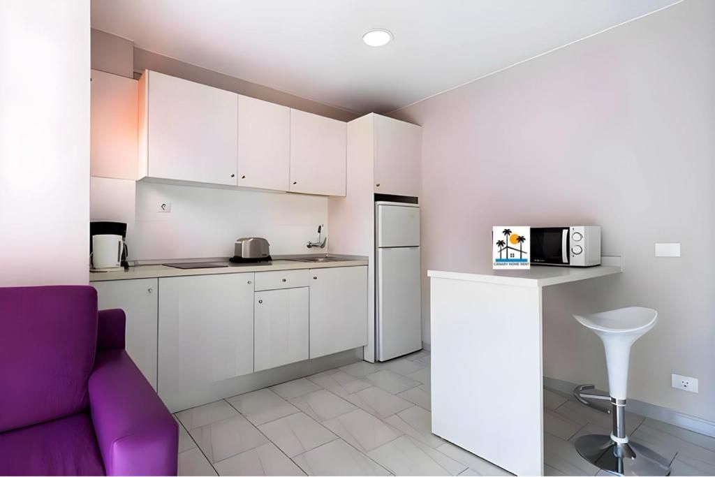 Una cocina con gabinetes blancos y una silla morada.