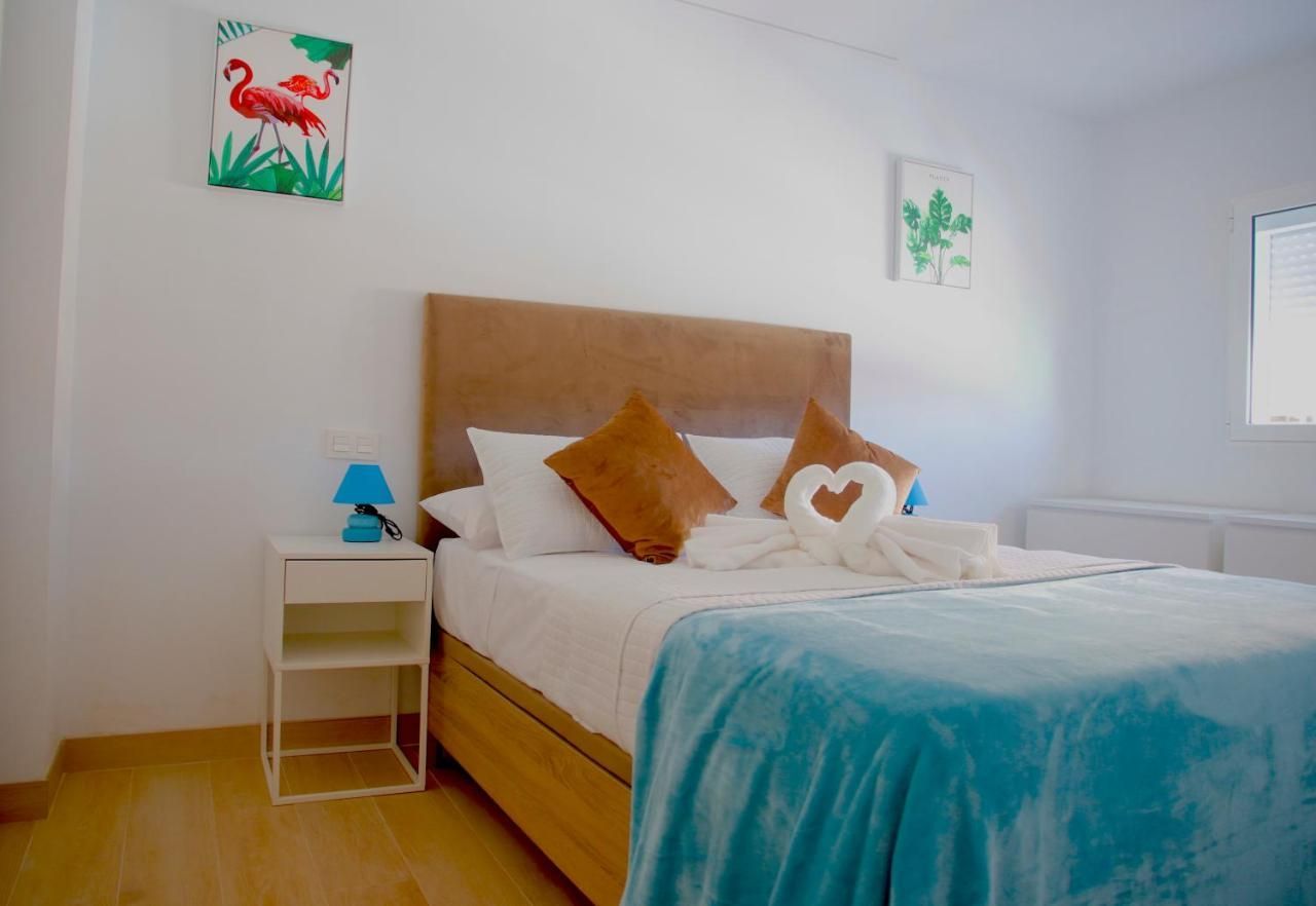 Un dormitorio con cama, mesita de noche, lámpara y cuadros en la pared.