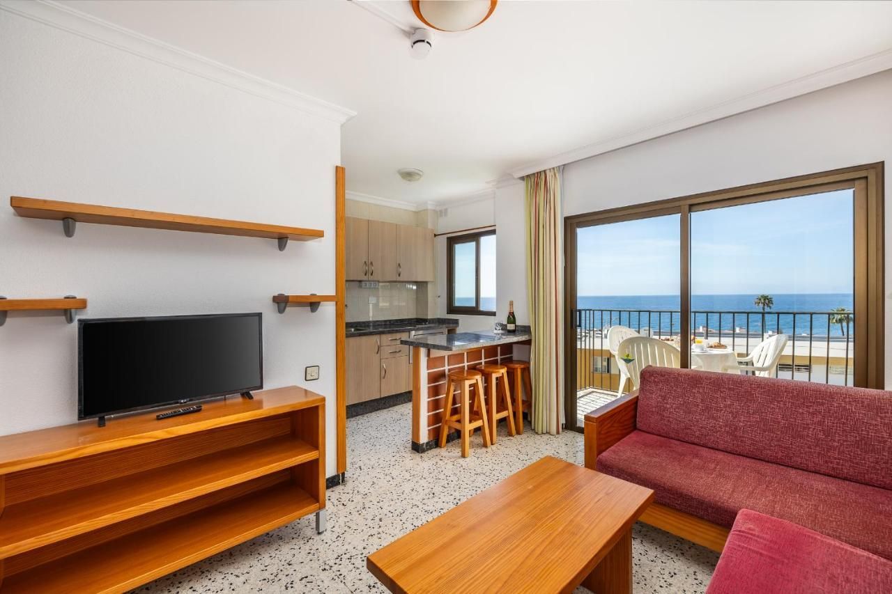 Una sala de estar con sofá, mesa, televisión y balcón con vista al mar.