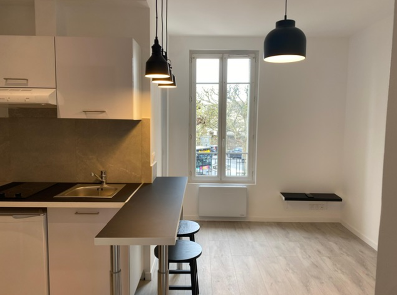 Kitchenette ouverte sur une pièce avec murs blancs et parquets au sol