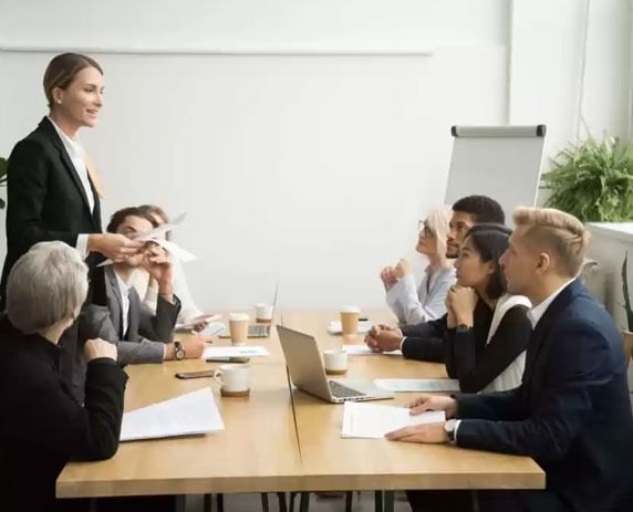 Una mujer está dando una presentación a un grupo de personas sentadas alrededor de una mesa.