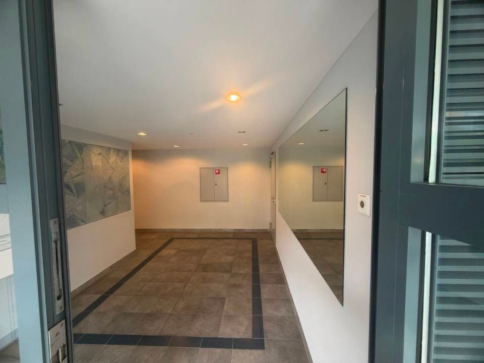 Entrée moderne vide avec sol carrelé, murs blancs, miroir mural et éclairage encastré au plafond.