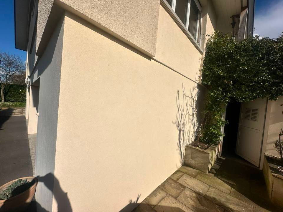 Côté d'une maison beige avec une allée pavée étroite et une plante en pot près de l'entrée