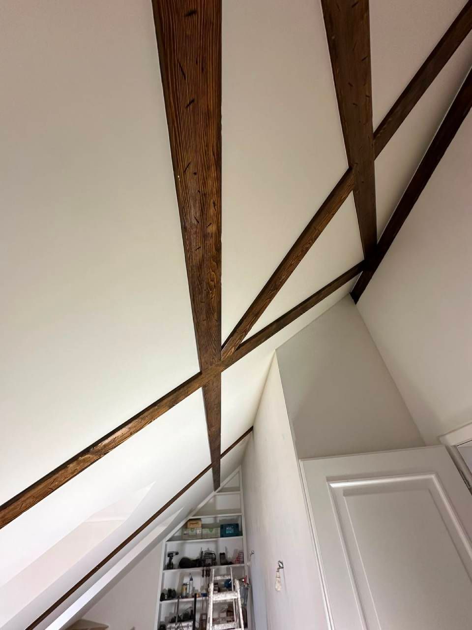 Plafond blanc incliné avec poutres apparentes en bois foncé au-dessus d'un escalier ou d'une ouverture de grenier