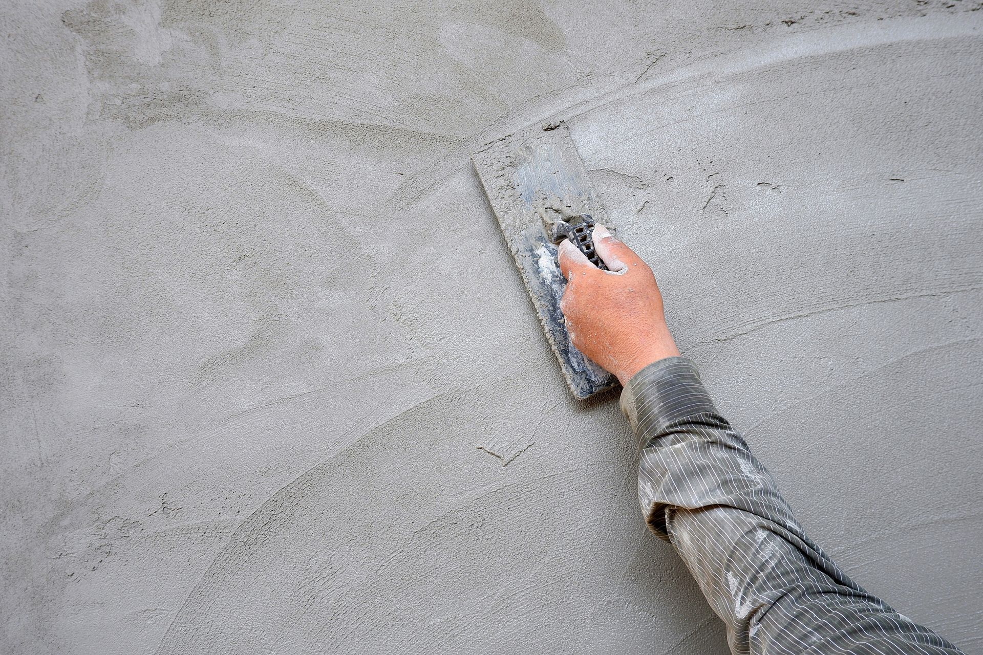Main gantée appliquant du plâtre blanc sur un mur à l'aide d'une truelle