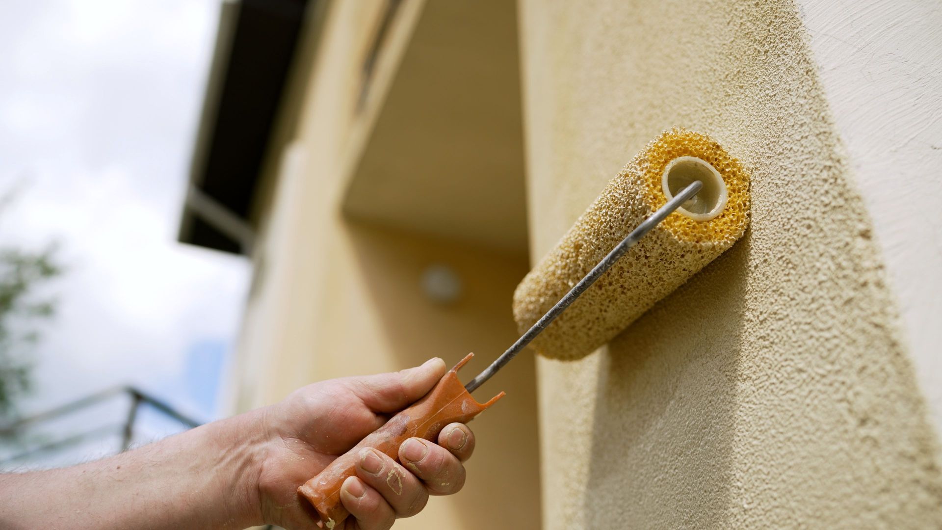 Une personne applique du plâtre gris sur un mur à l'aide d'une truelle, tout en portant des gants blancs et des vêtements de travail.