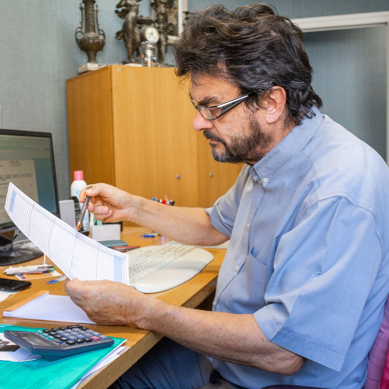 Un homme portant des lunettes examine des documents à un bureau, dans un environnement de bureau.