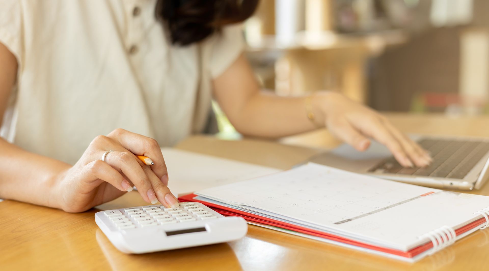 Une femme utilise une calculatrice, un cahier et un ordinateur portable sur un bureau en bois.