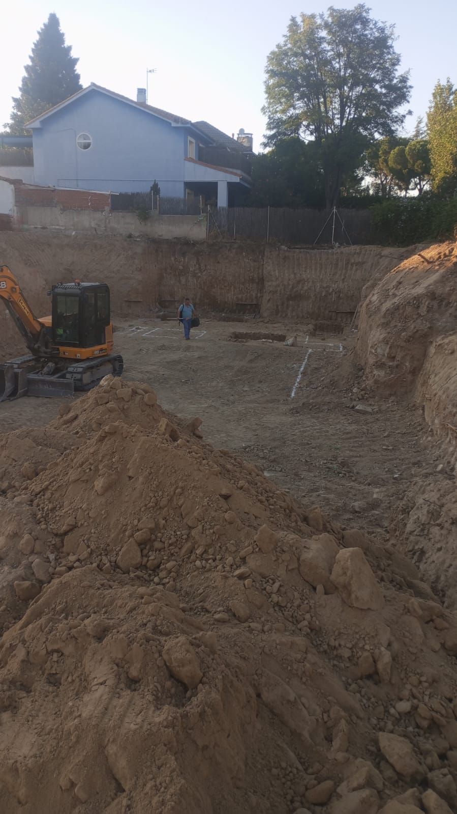 Un sitio de construcción con un gran montón de tierra y una casa al fondo.
