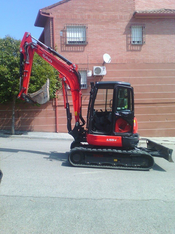 Una excavadora roja está estacionada frente a un edificio de ladrillos.