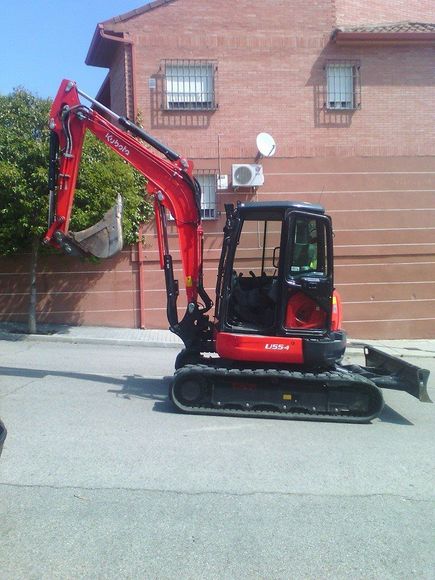 Una excavadora roja está estacionada frente a un edificio de ladrillos.