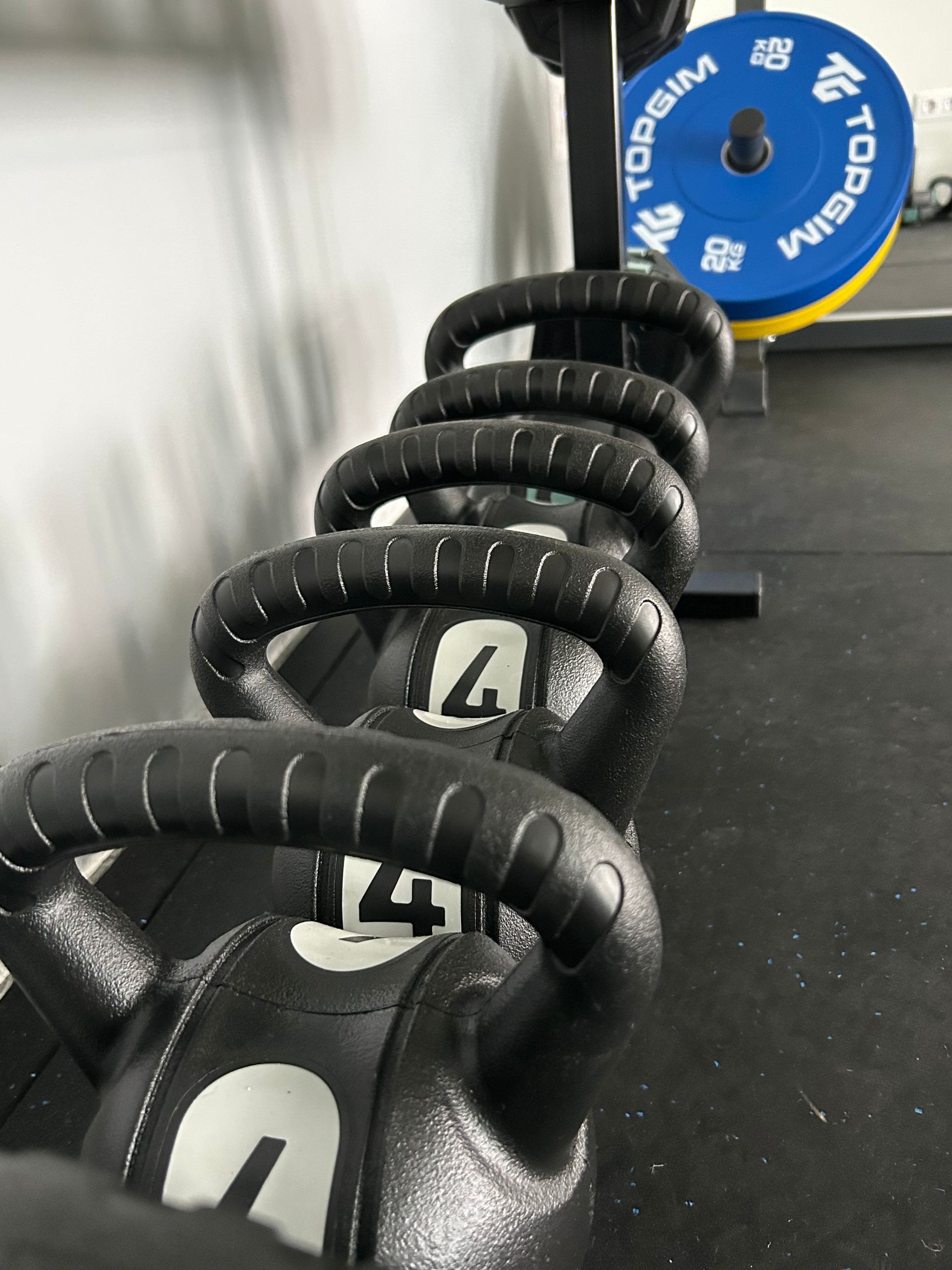 Dos mancuernas azules de 2 kg, una báscula, una pelota y zapatos sobre una superficie blanca, lo que sugiere un equipo de fitness.