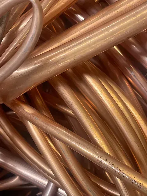 Tubos de cobre, de distintas longitudes, entrelazados, con superficie pulida y reflectante.