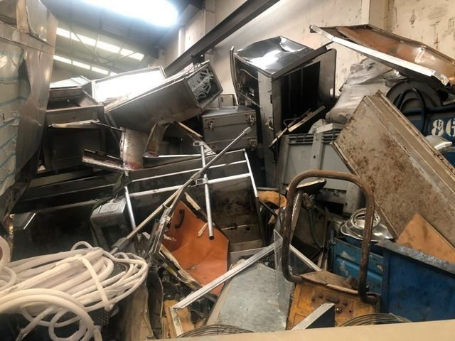 Pila de chatarra que incluye electrodomésticos, piezas y cables dentro de un edificio.