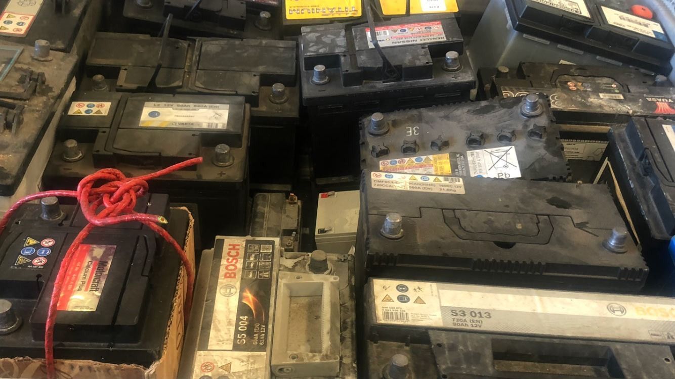 Pila de baterías de coche negras, algunas con etiquetas y cuerda roja.