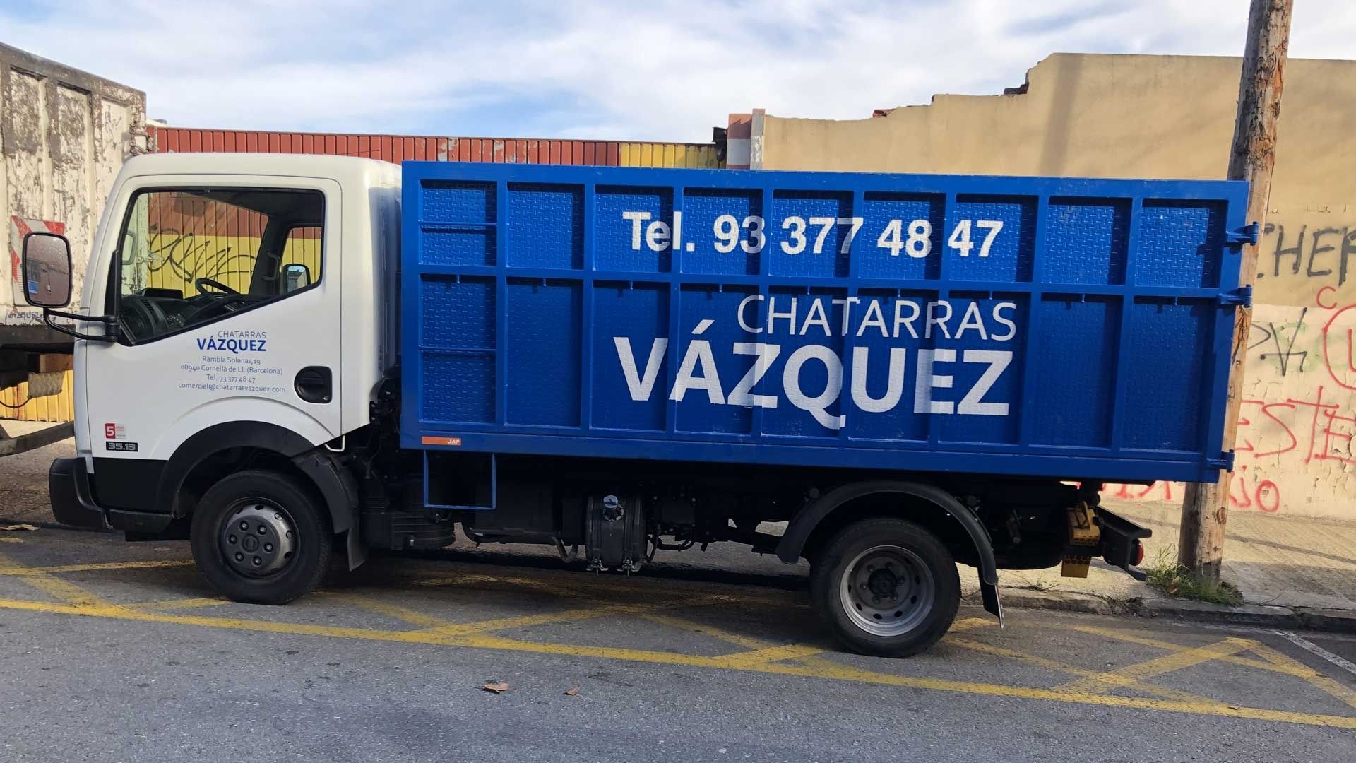 Camión de chatarra azul y blanco estacionado en una calle; dice