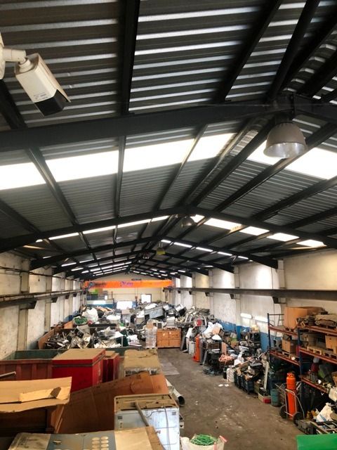 Interior de almacén lleno de artículos desordenados bajo un techo de metal con tragaluces e iluminación cenital.