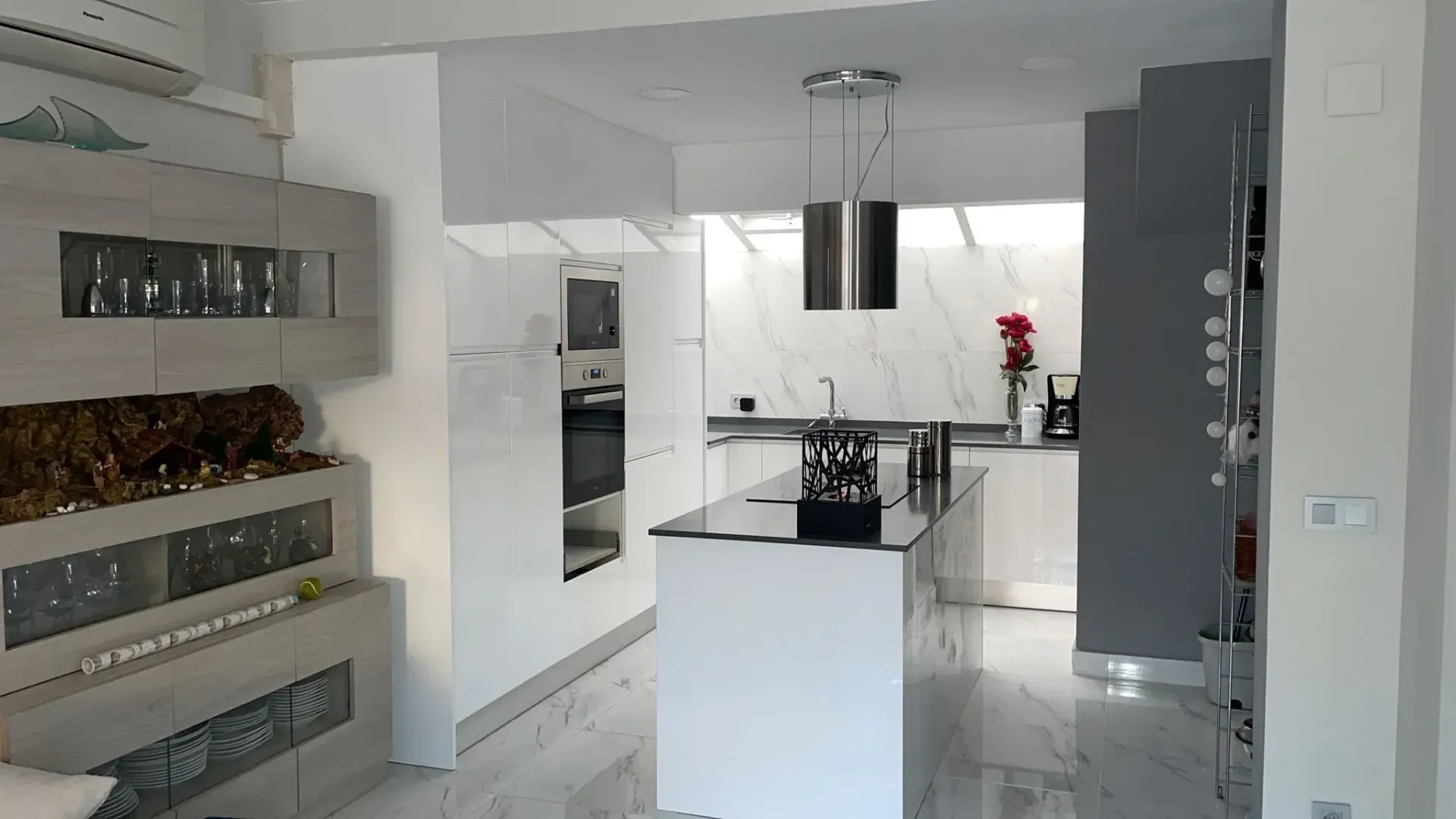 Cocina blanca moderna con isla, salpicadero de mármol y electrodomésticos empotrados.