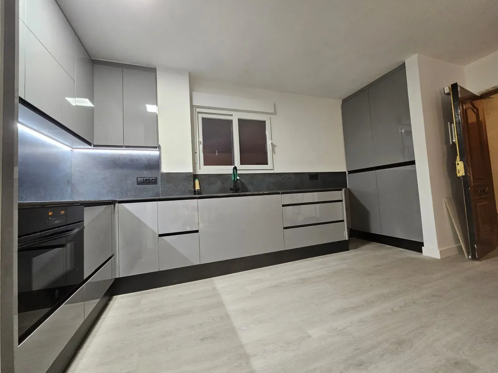 Cocina gris moderna con gabinetes, electrodomésticos, encimeras oscuras y pisos con apariencia de madera clara.