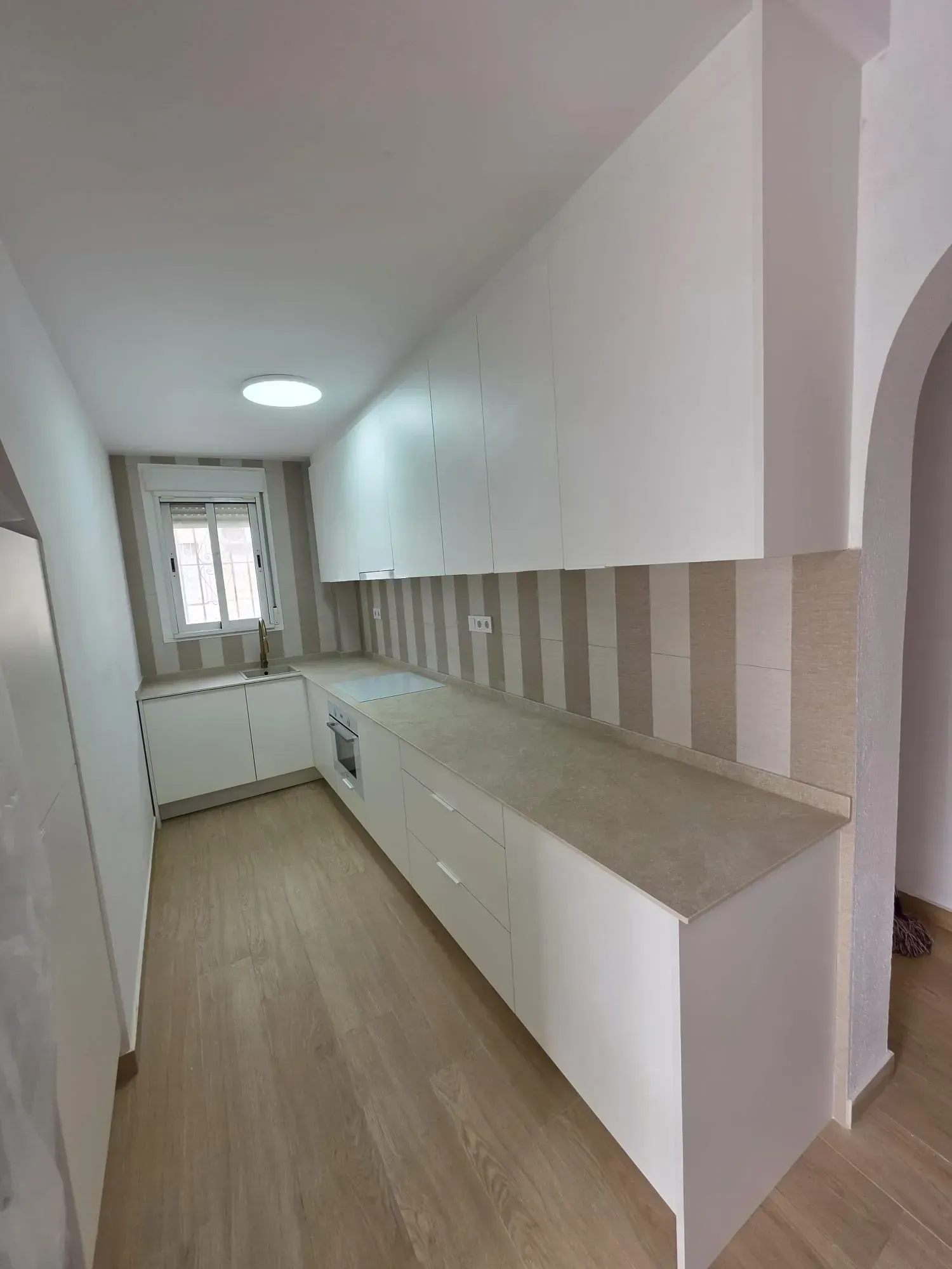 Cocina blanca con encimera larga y armarios a juego. Revestimiento a rayas y suelo de madera.