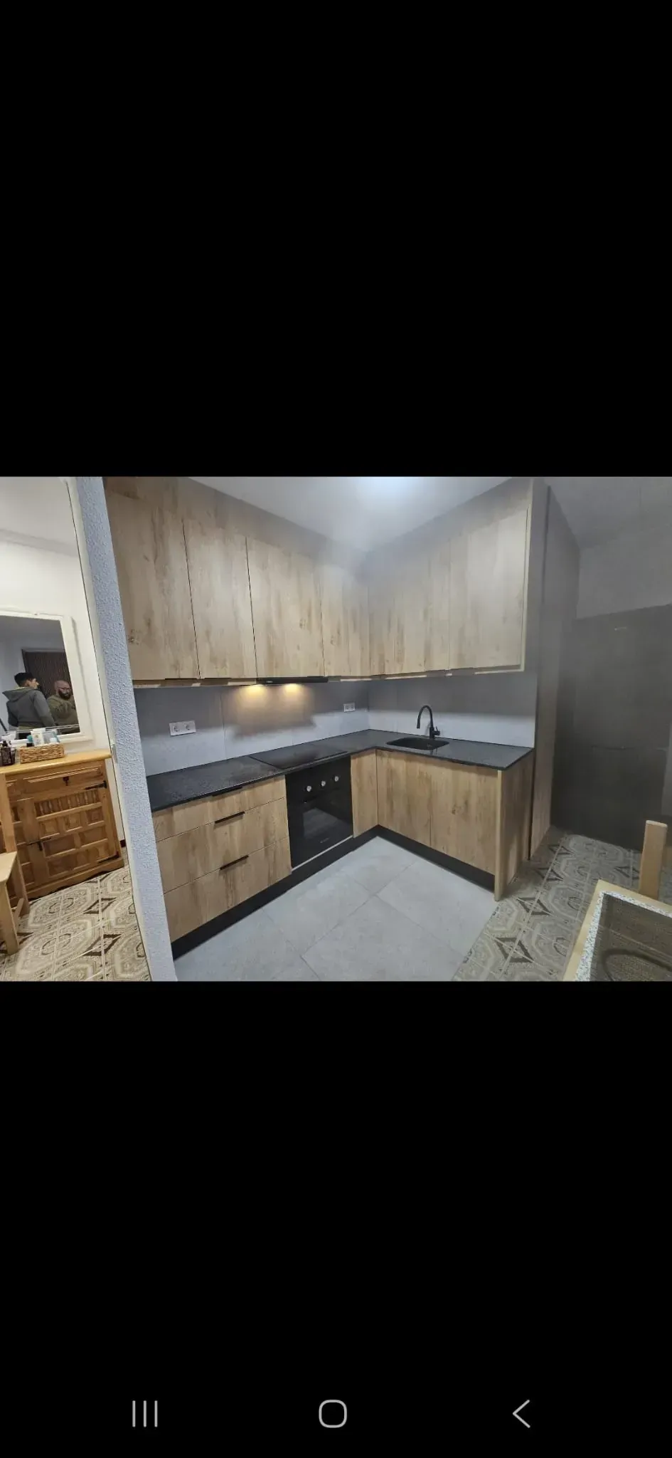 Una cocina moderna con gabinetes de madera clara, encimeras oscuras y un horno negro.